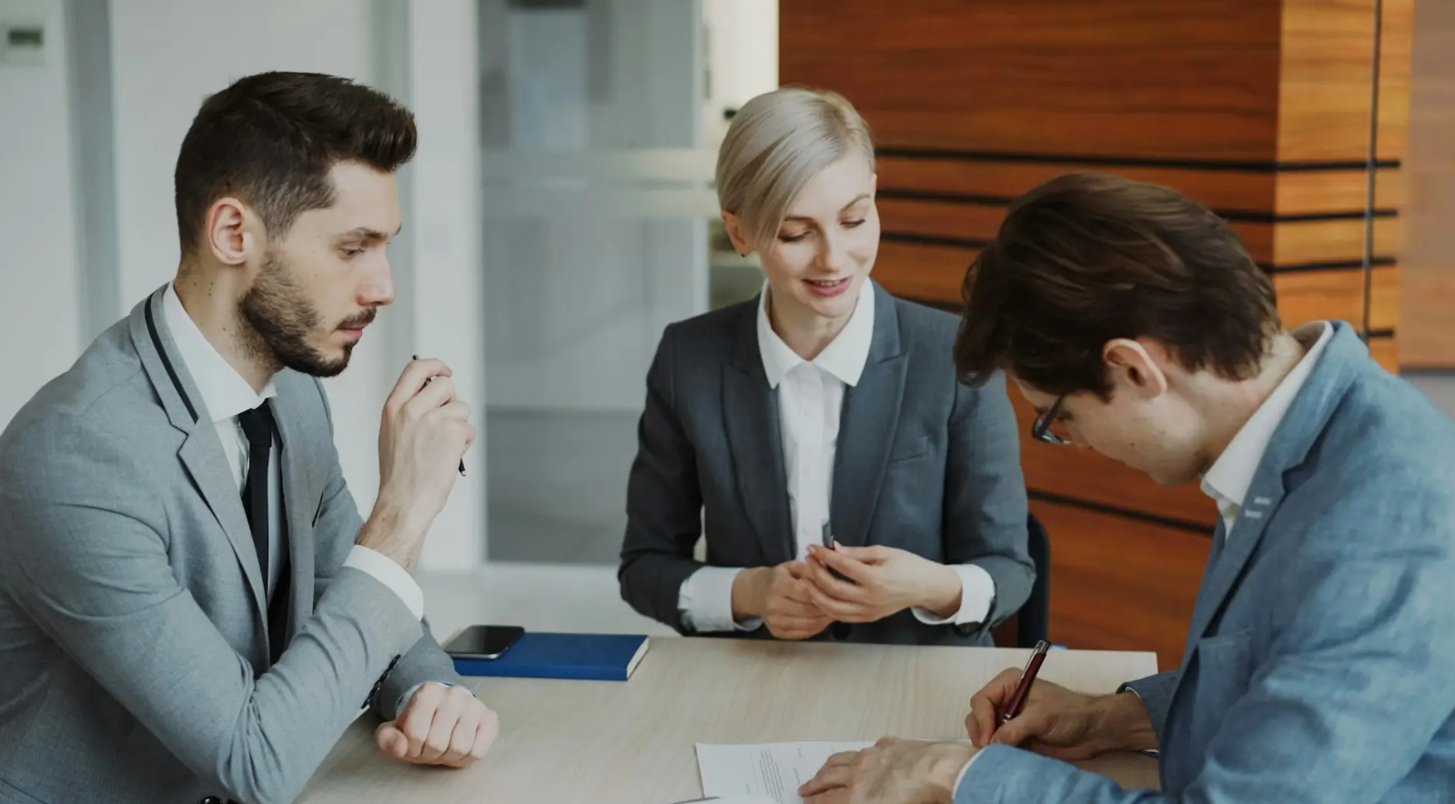 Three business professionals reviewing and signing documents at a table.