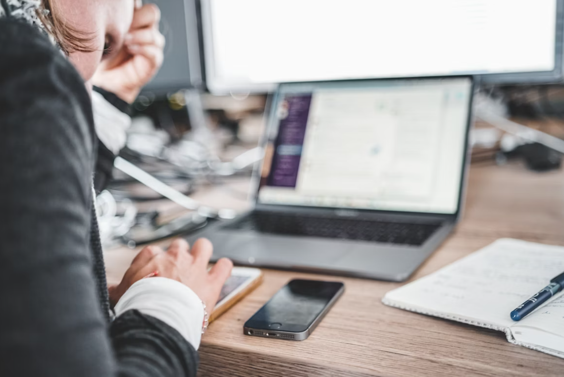 Person working on a laptop with phone and notepad on desk.