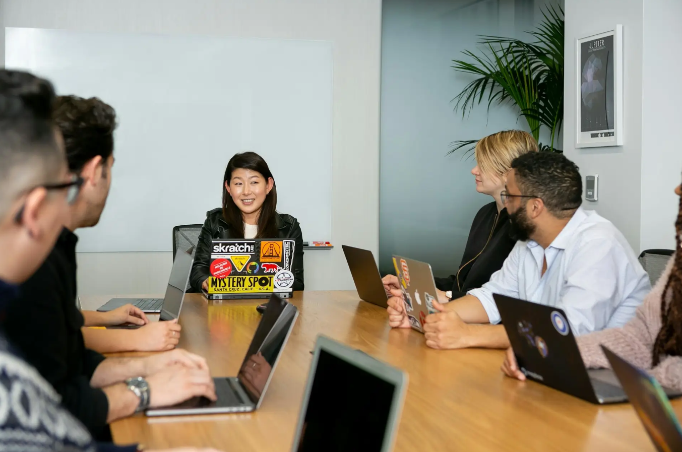 Team in a meeting room discussing ideas around a conference table with laptops.