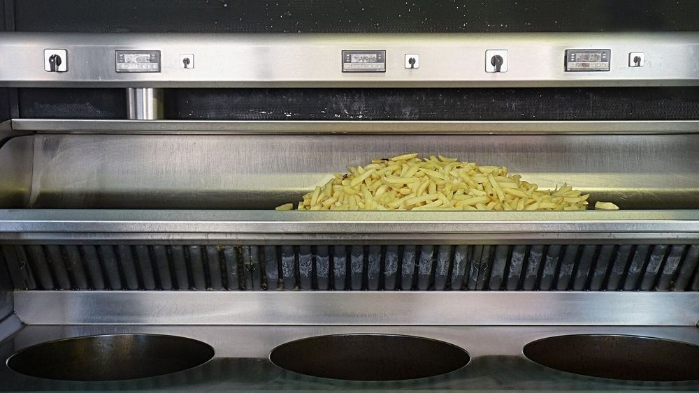 A stainless steel commercial chip-shop fryer with a batch of fries in the holding tray