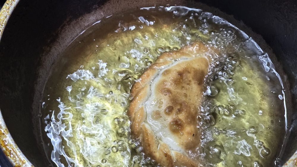 A golden beef empanada deep frying in a pot of bubbling hot fat