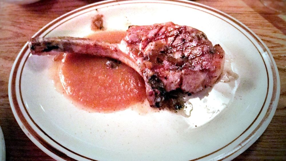 Seared bone-in pork chop with applesauce on a white plate
