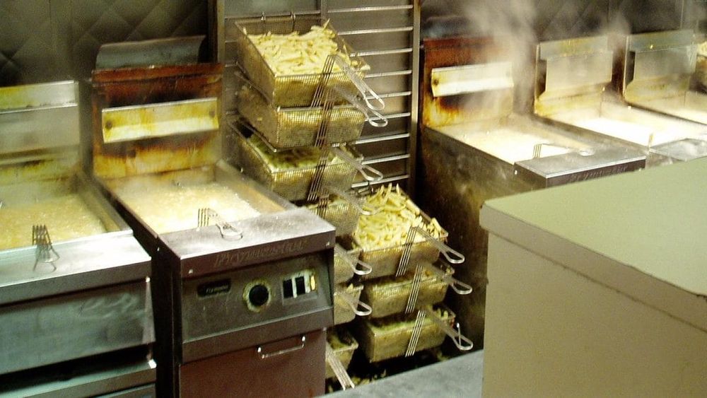 Wire baskets of French fries beside commercial deep fryers in a restaurant kitchen