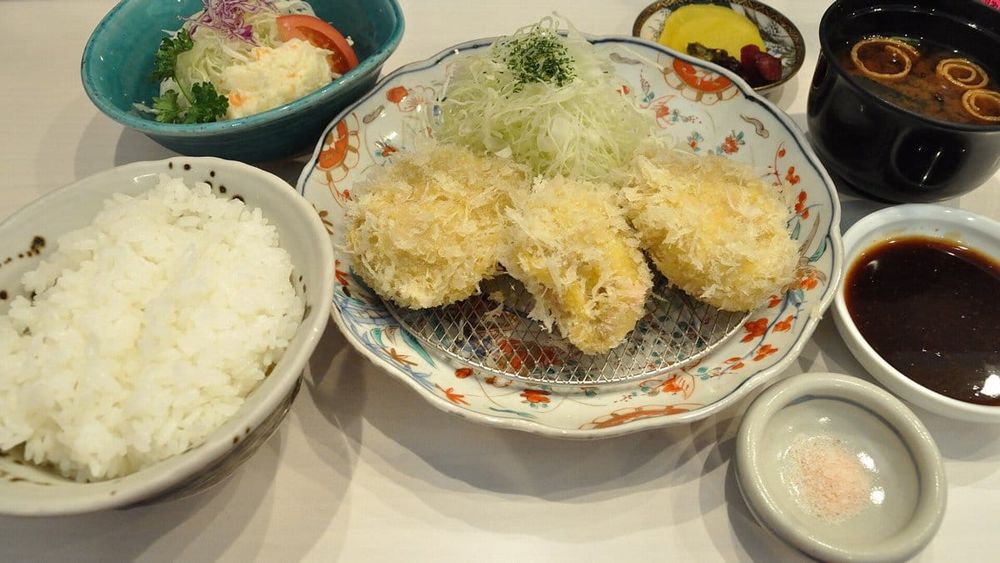 Golden panko-crumbed pork cutlets on a wire rack with shredded cabbage, rice, miso soup and tonkatsu sauce