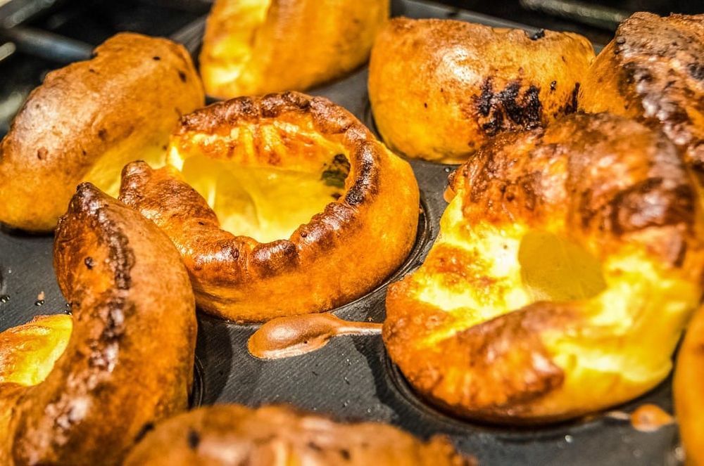 Golden Yorkshire puddings risen tall in a dark 12-hole tin, baked in beef dripping