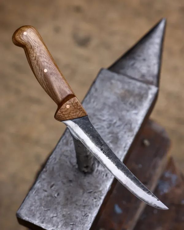 A long bladed knife with a wooden handle resting on an anvil.