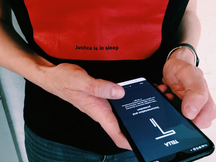 Someone wearing a T-shirt that says "Justice is in sleep" holds a phone with Tella opened 