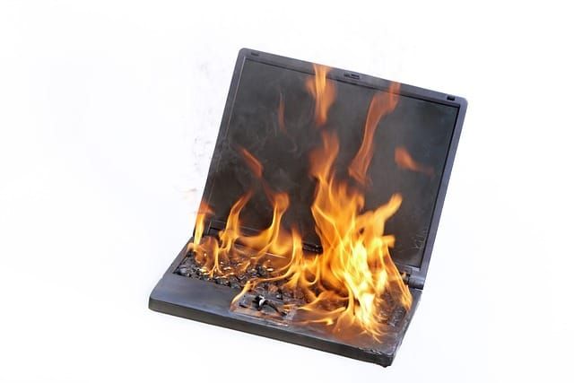 A black laptop, on fire and melting, against a white background