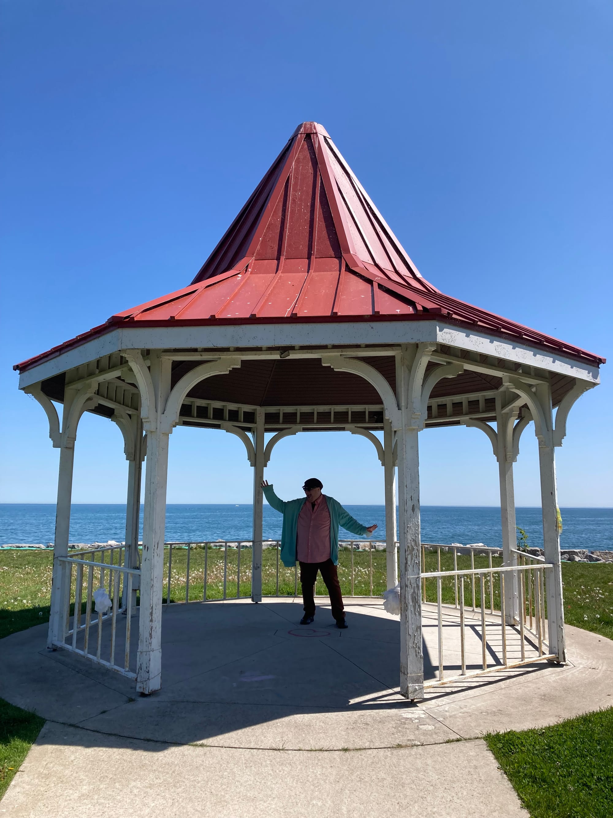 Jonathan posing under the red-roofed gazebo in Long Branch Park, framed by the deep blue of the sky and Lake Ontario.
