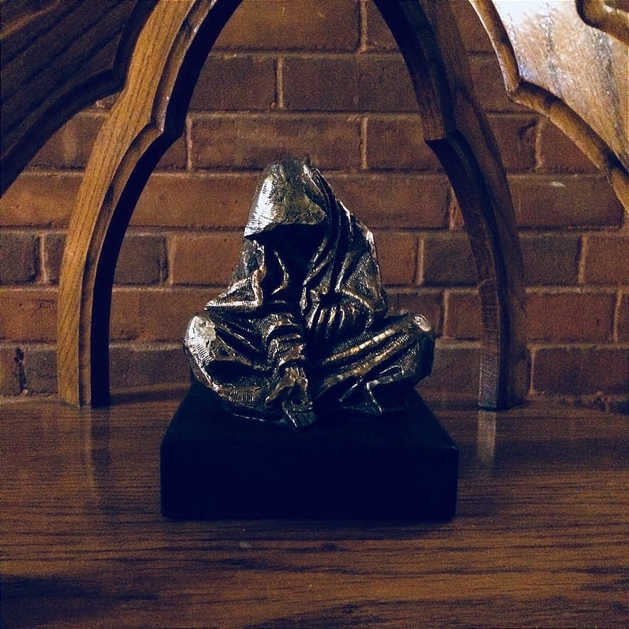 A statue of a seated hooded figure, with one hand outstretched.