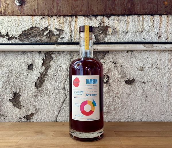 A bottle of Ortolan Damson Plum Liqueur by Pekut and Carwick Independent Bottlers and Appanage Brands against a textured concrete background.