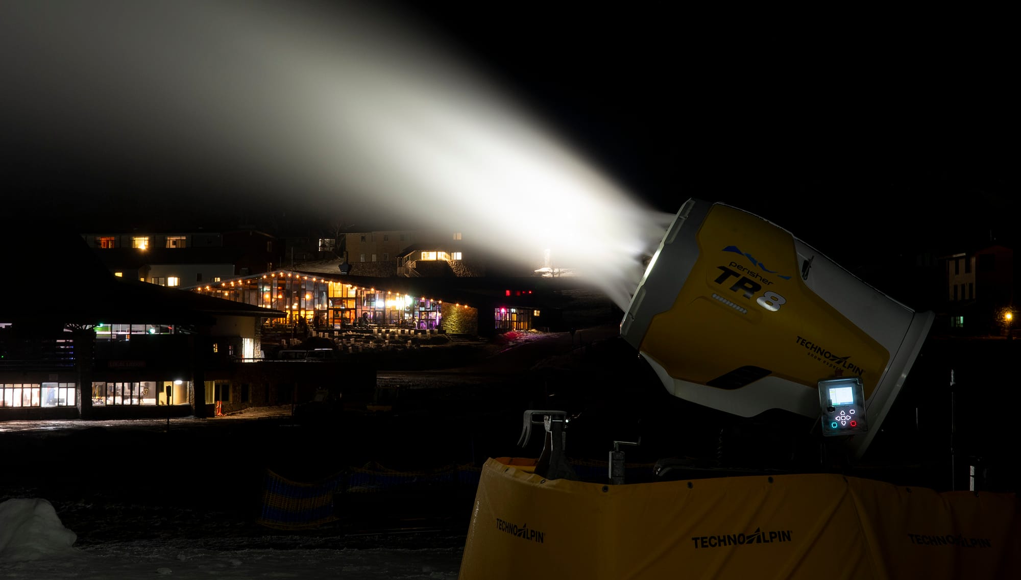 A snow gun in Front Valley with hotels in the background.