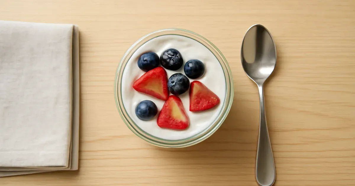 Glass jar of lactose-free yogurt topped with fresh strawberries and blueberries as a low FODMAP snack