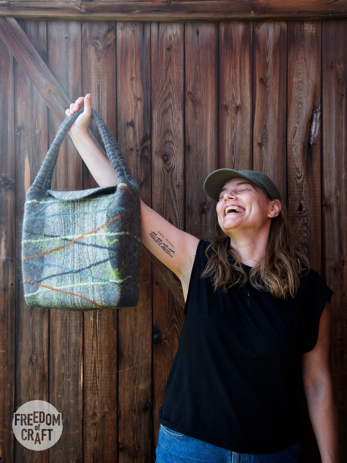 A woman is lifting her finished bag in the air. Happy and proud. The bag is grey, adorned with threads.