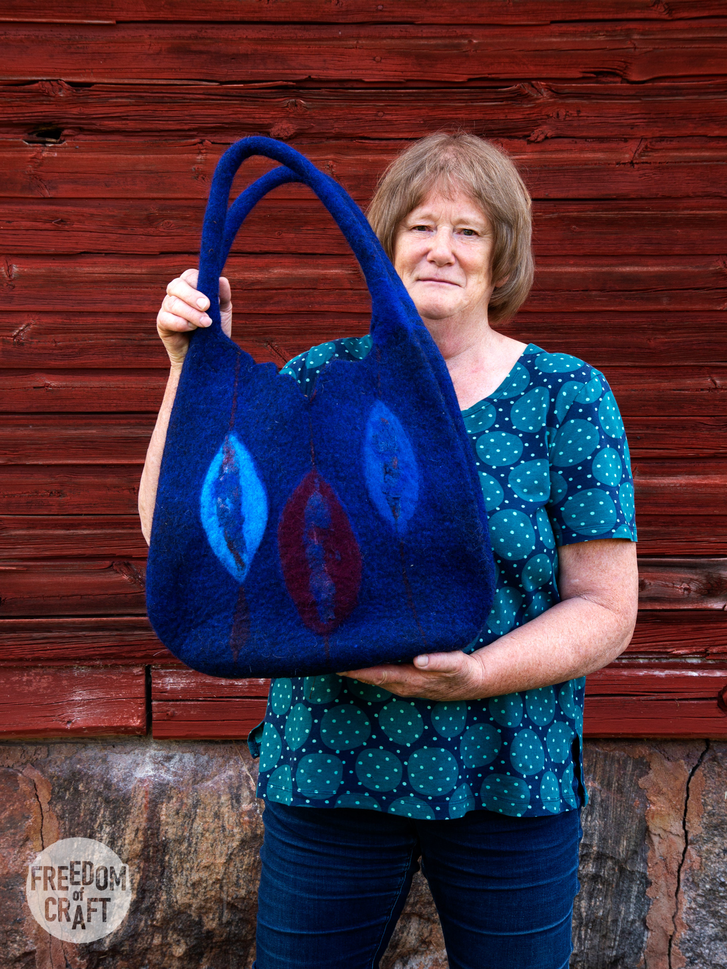 A woman dressed in blue, is holding up her finished bag, which is alslo blue. Matching her clothes.