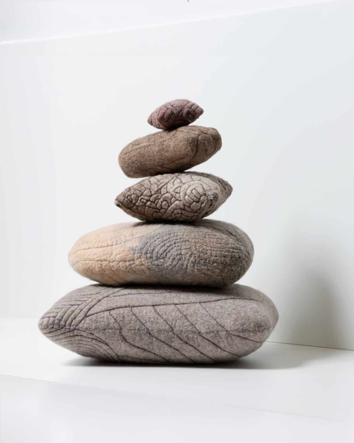 Felted cushions stacked on a pile in soft grey colours.