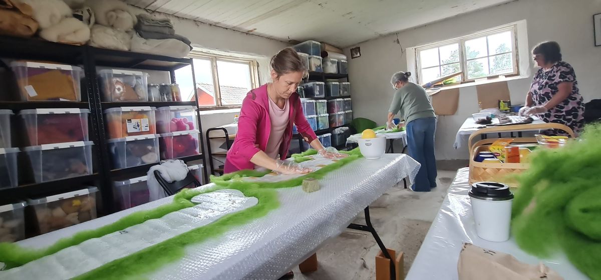 En kvinna i rosa arbetar med sitt skoprojekt. Grön ull ligger under en mall i plast.