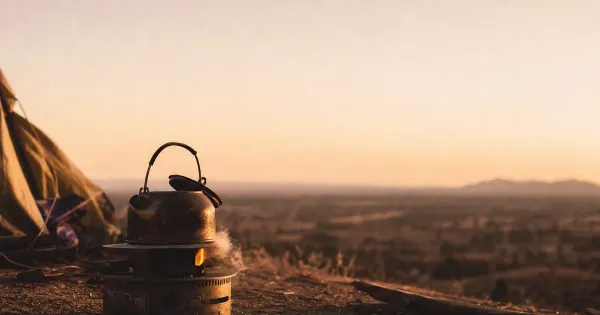 Bollitore su fornello freddo, coperchio storto, in una radura da campeggio, al primo minuto del tramonto, hai bug mentale