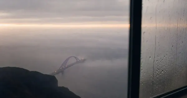 Arco di ponte che emerge dalla nebbia, accanto a una finestra con scie di pioggia, sotto un velo sottile di nuvole, idee…