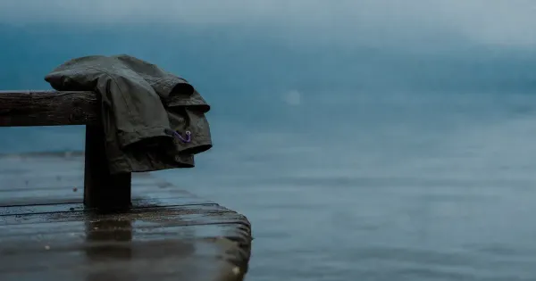 Impermeabile piegato su panchina, orlo umido, su un molo sull'acqua calma, all'ora blu, importanza formazione continua