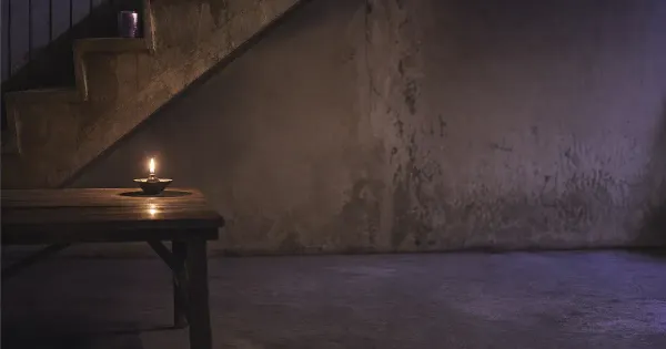 Fiamma solitaria su tavolo ampio e vuoto, sotto una scala di cemento, nel silenzio profondo d'estate, mito giorni bugia