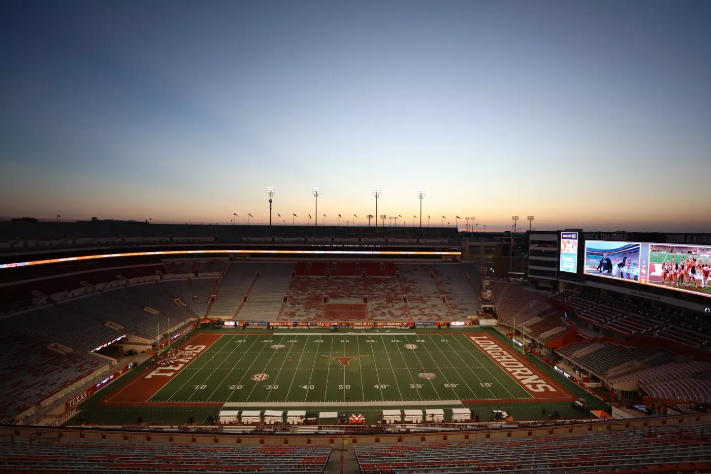 Texas Memorial Stadium in Austin at dusk, with the field and video board lit