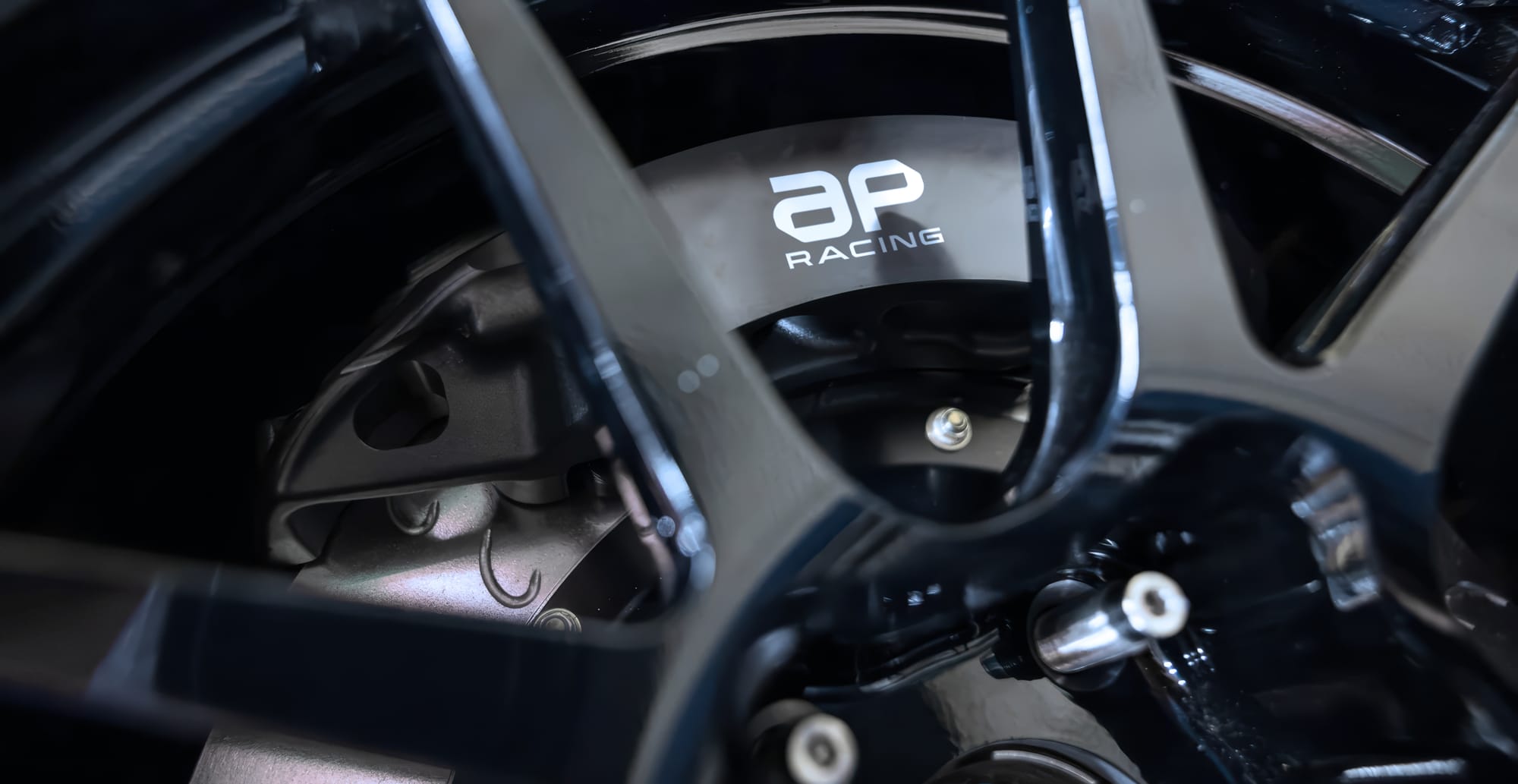 AP Racing brake caliper displaying the company's new logo behind a performance alloy wheel.