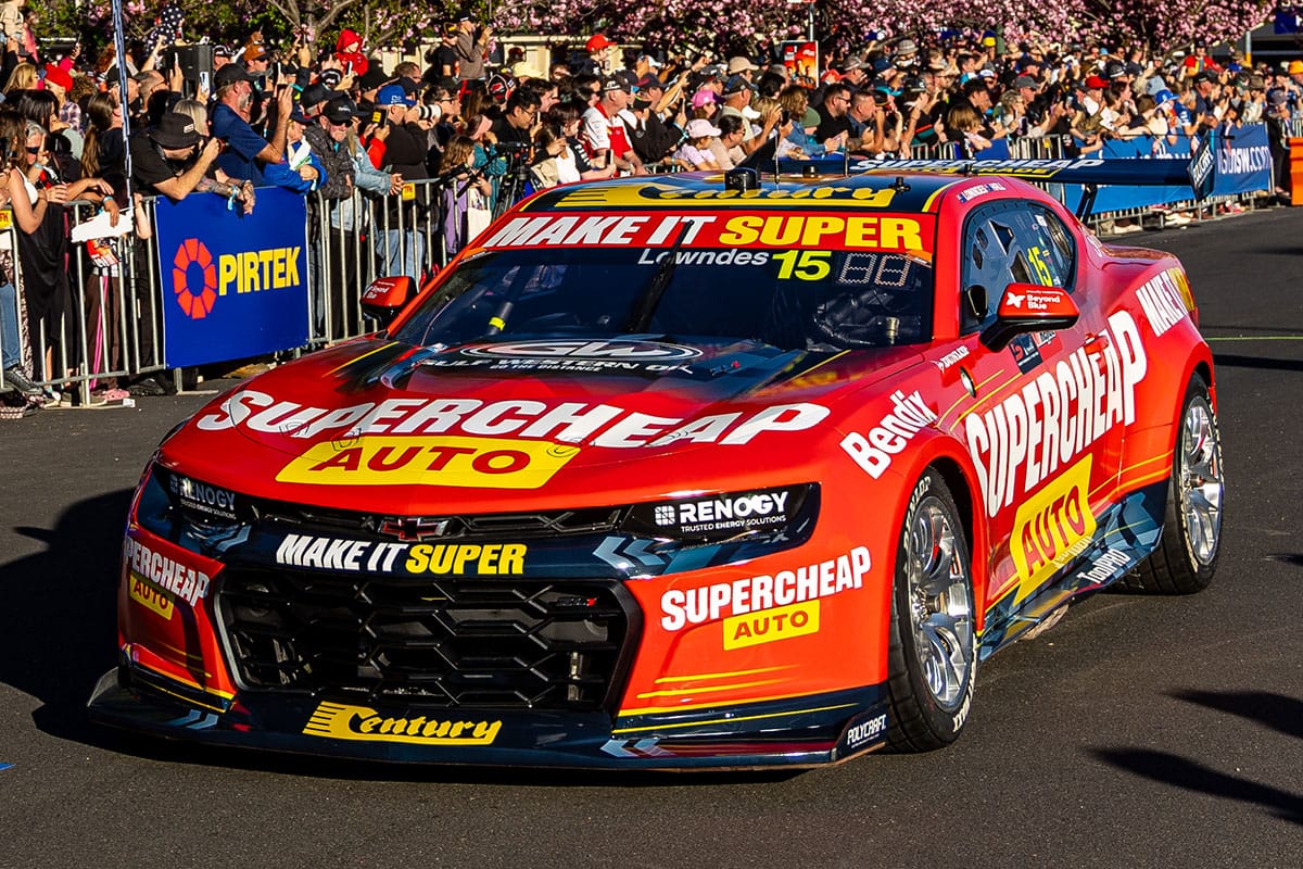 Red and yellow number 15 Chevrolet Camaro Supercar in Supercheap Auto livery driven past a large crowd at a street parade.