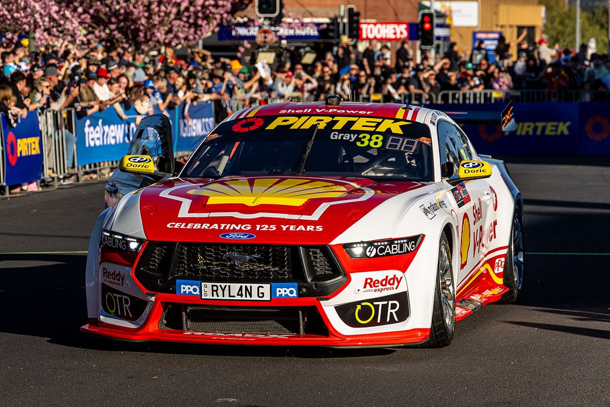 Red, white and yellow number 38 Ford Mustang Supercar in Shell livery driven past a cheering crowd at a street parade.