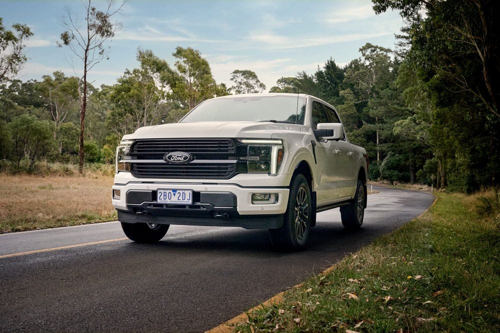 White Ford F-150 Platinum pickup on a tree-lined country road