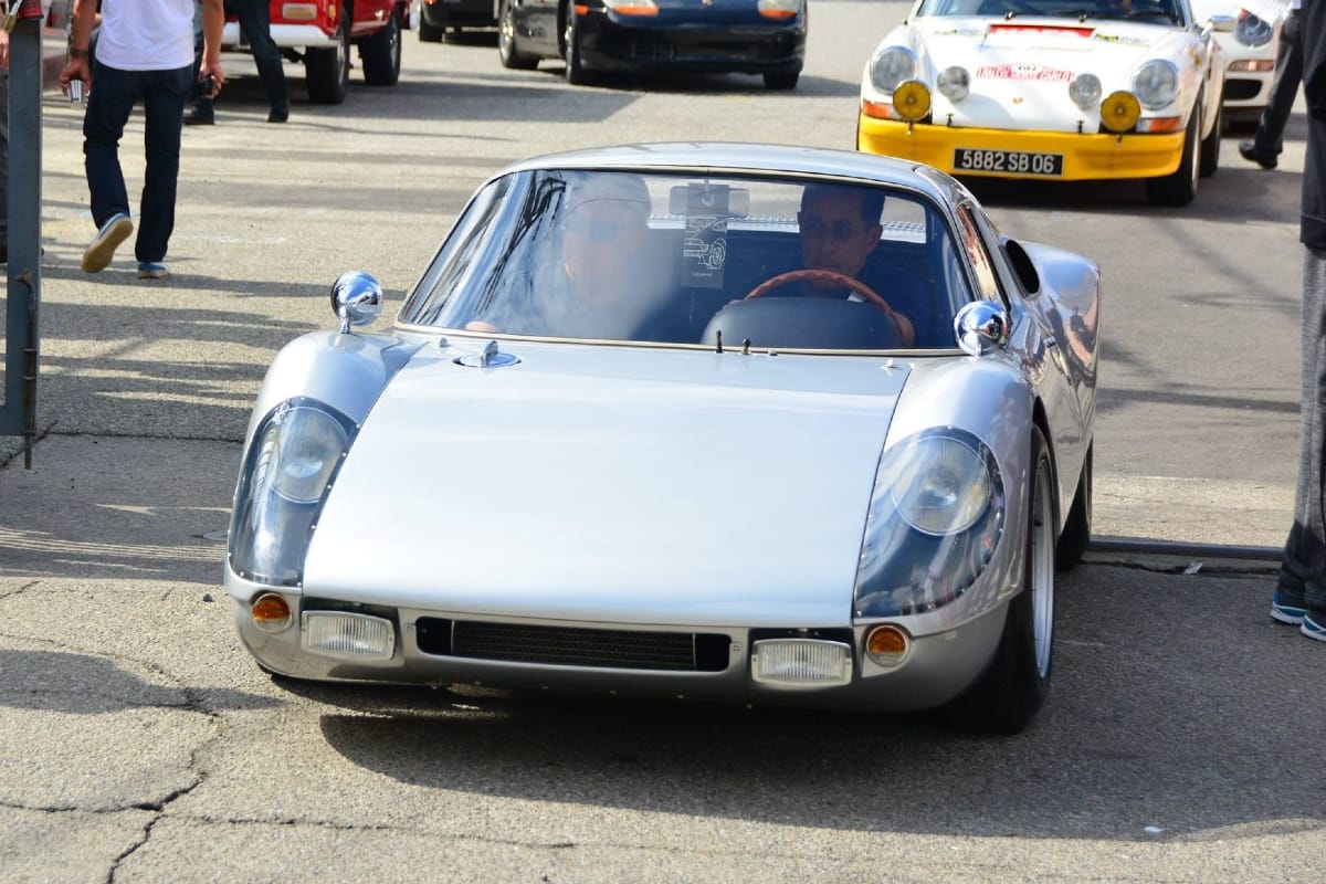 Silver Porsche 904 Carrera GTS coupe driving through a classic car event paddock