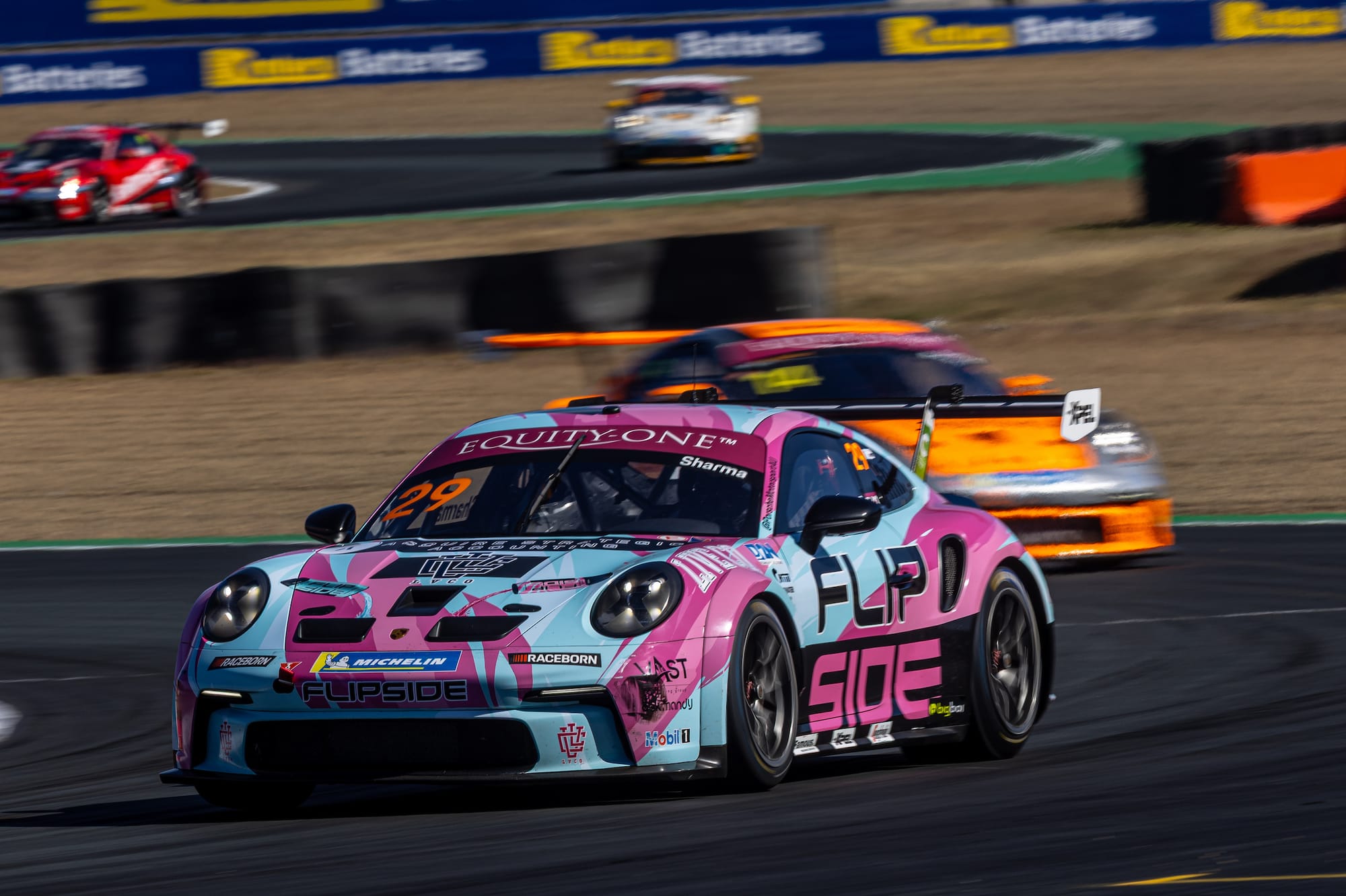 FLIPSIDE number 29 Porsche 911 GT3 Cup race car cornering ahead of an orange Porsche, with more race cars on the track behind.