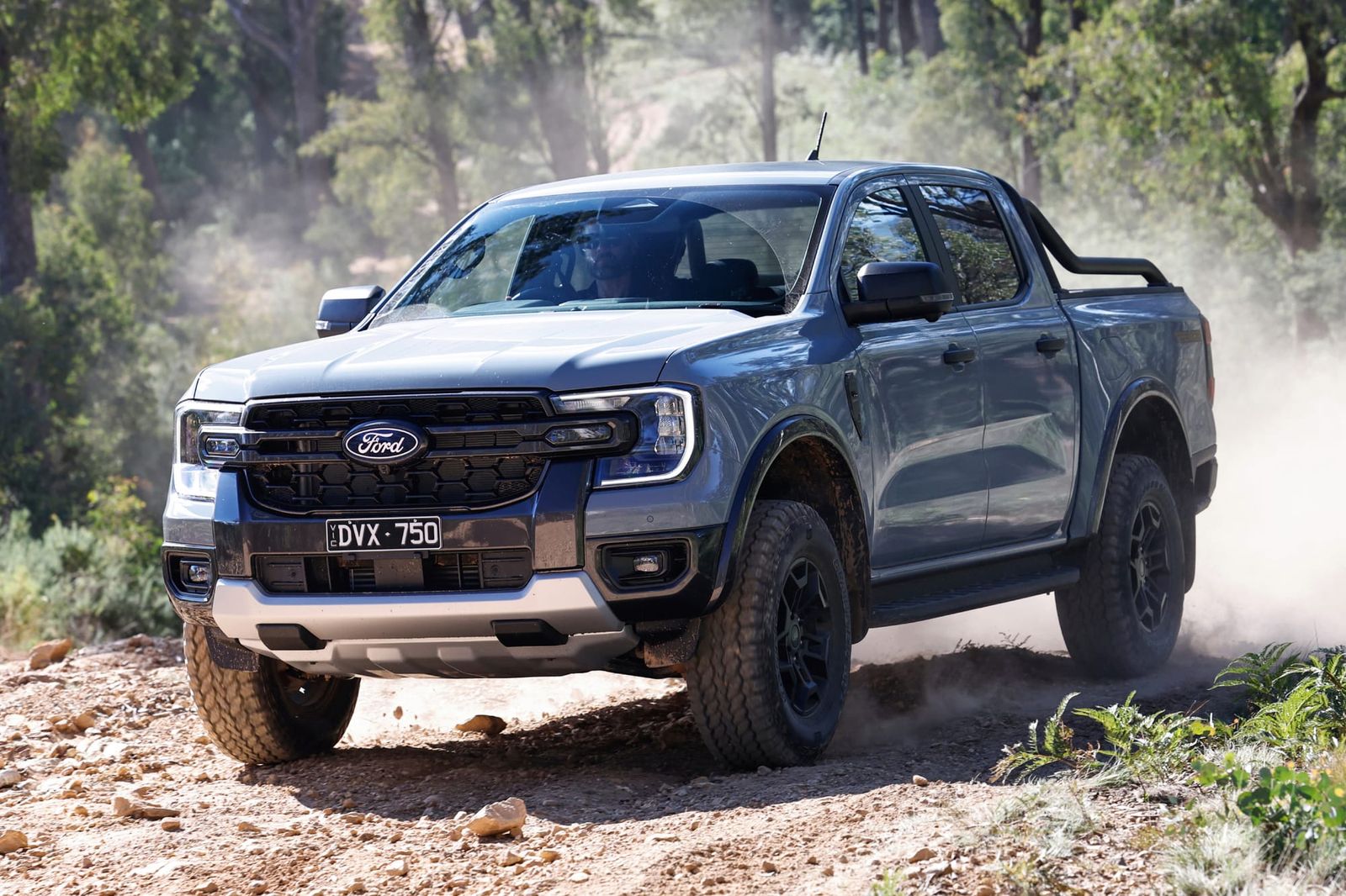 Grey Ford Ranger Tremor ute with a sports bar driving over rocky dirt, kicking up dust