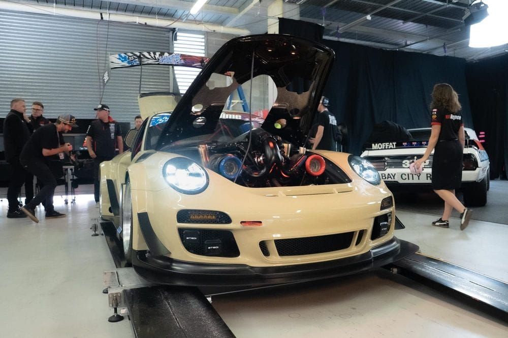 Sandy Taupe Porsche 911 wide-body with its front bonnet open revealing a twin-turbo V8