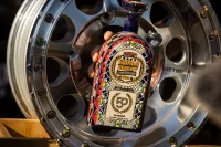 Close-up of a hand placing a colourful ceramic SCORE World Desert Championship trophy in the centre of a polished Method Race Wheels beadlock wheel.