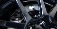 AP Racing brake caliper displaying the company's new logo behind a performance alloy wheel.