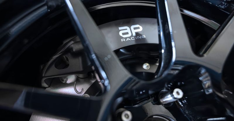 AP Racing brake caliper displaying the company's new logo behind a performance alloy wheel.