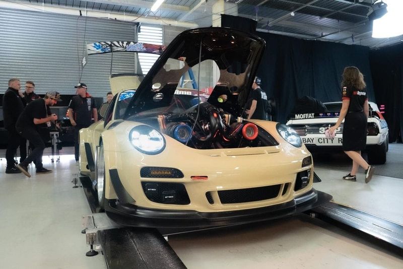 Sandy Taupe Porsche 911 wide-body with its front bonnet open revealing a twin-turbo V8