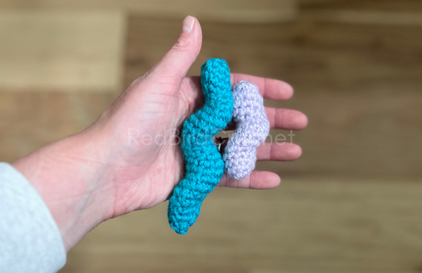 Close-up of two handmade crochet Whirly Marble Fidgets. They are tubes with a marble crocheted inside that twist. 