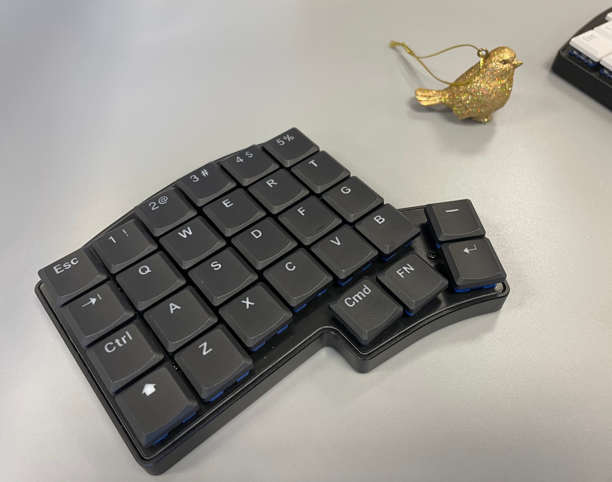 Left half of a Keebio Iris LM next to a very round golden bird ornament