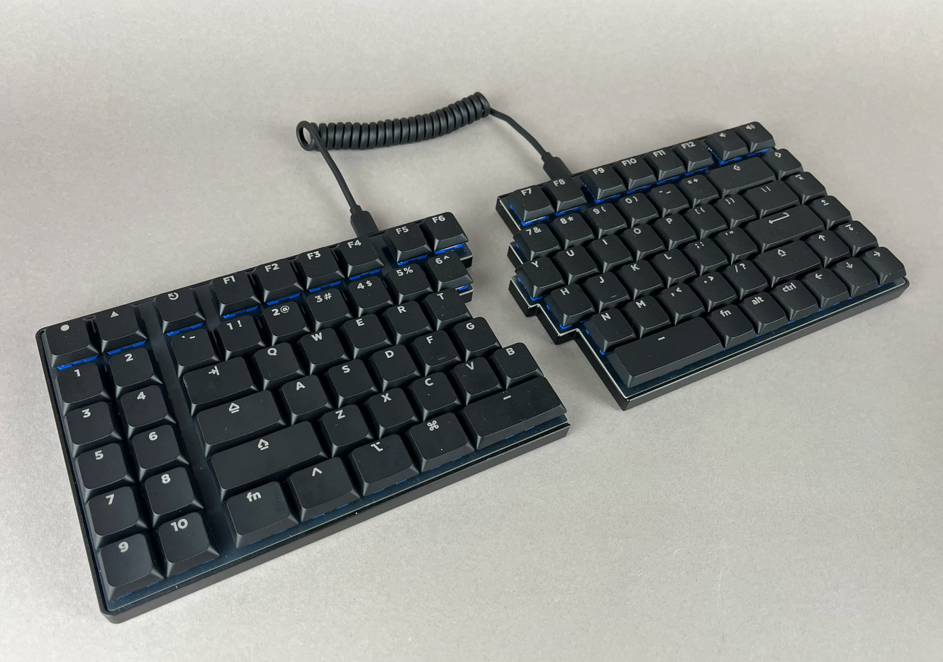 Pictured: the Sinc LM, which is a 75% TKL split mechanical traditional row stagger keyboard with a macro section and function row. It has Deep Sea Mini Whale Silent Tactile switches for whisper-quiet typing and is connected by a coiled USB-C cable. It has LPF Legend Glow shine through keycaps covering the board.
