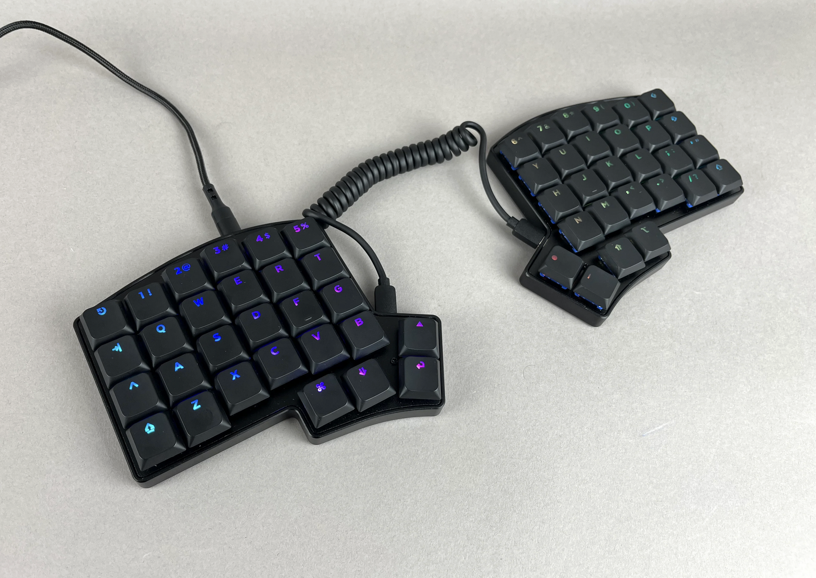 The Iris LM is pictured with the Deep Sea Mini Whale Silent Tactile switches with the LPF Legend Glow keycaps and a coiled cable to connect the halves.