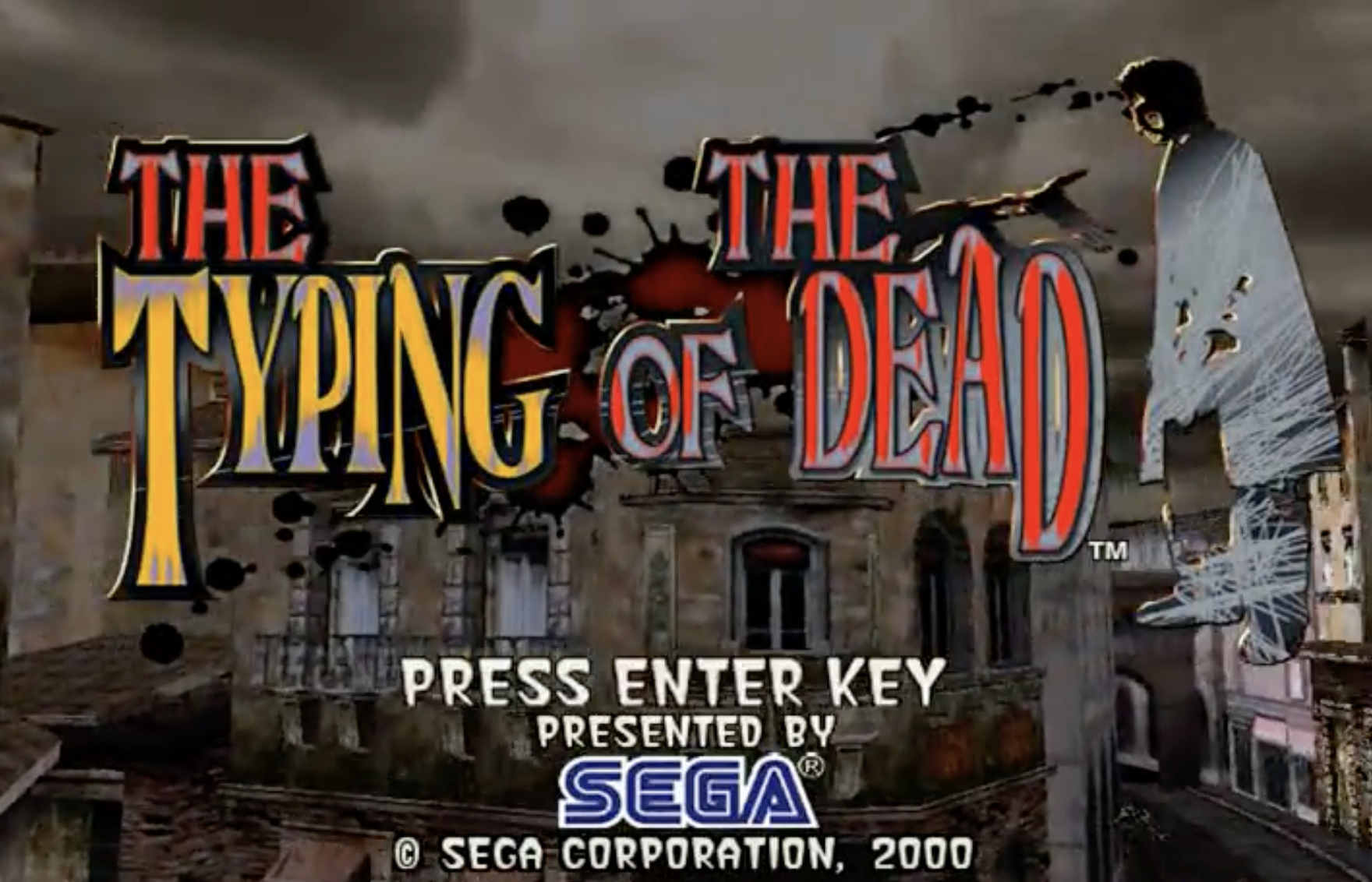 Screen capture of the opening of "The Typing of the Dead," complete with dilapidated buildings and a deep gray cast sky. A blood spatter serves as the immediate backdrop for the title, with a request for the gamer to press the Enter Key. Presented by Sega.