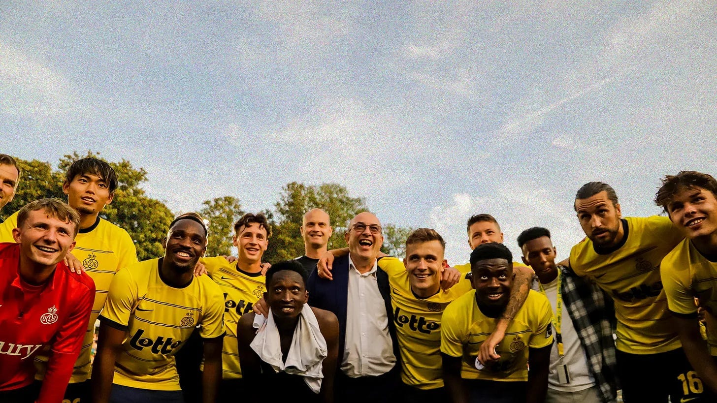 A photo of Royale Union Saint-Gilloise's squad huddled together, taken from below, set against a blue summer sky