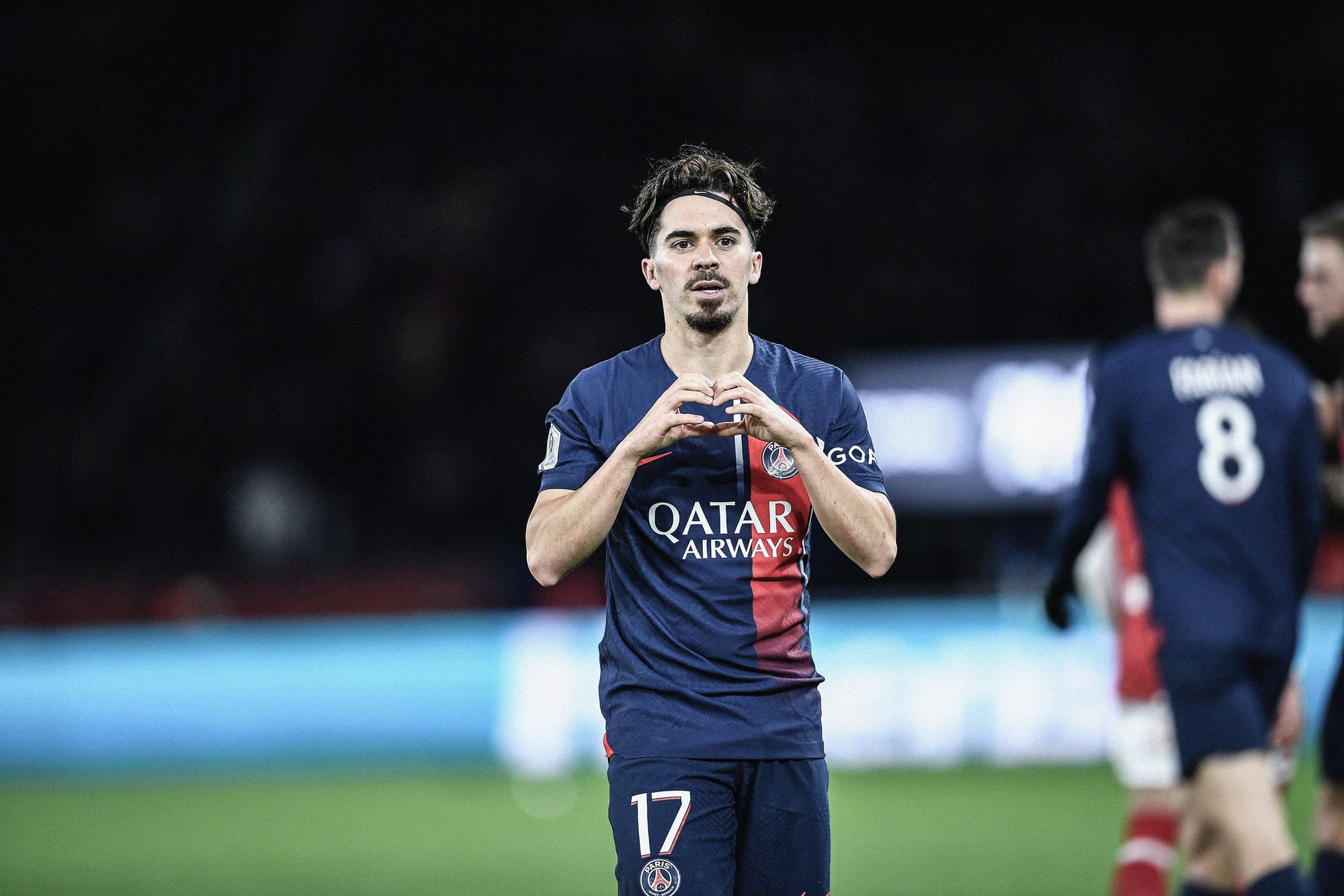 A photo of Vitinha in a navy blue Paris Saint-Germain shirt making a heart gesture with his hands