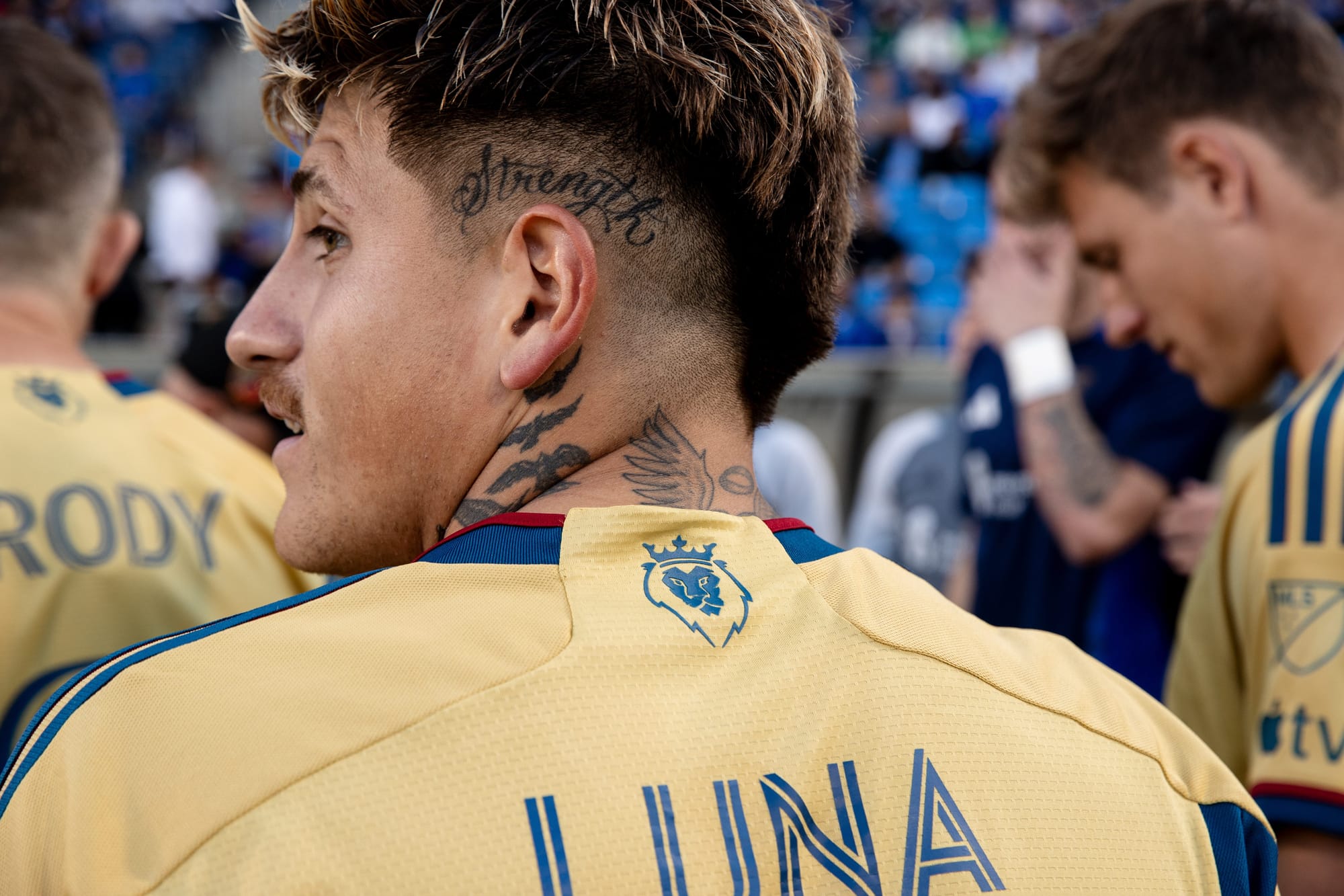 Close-up of Diego Luna from behind, showing the details of his tattoos on his neck and side of head, as well his gold Real Salt Lake kit