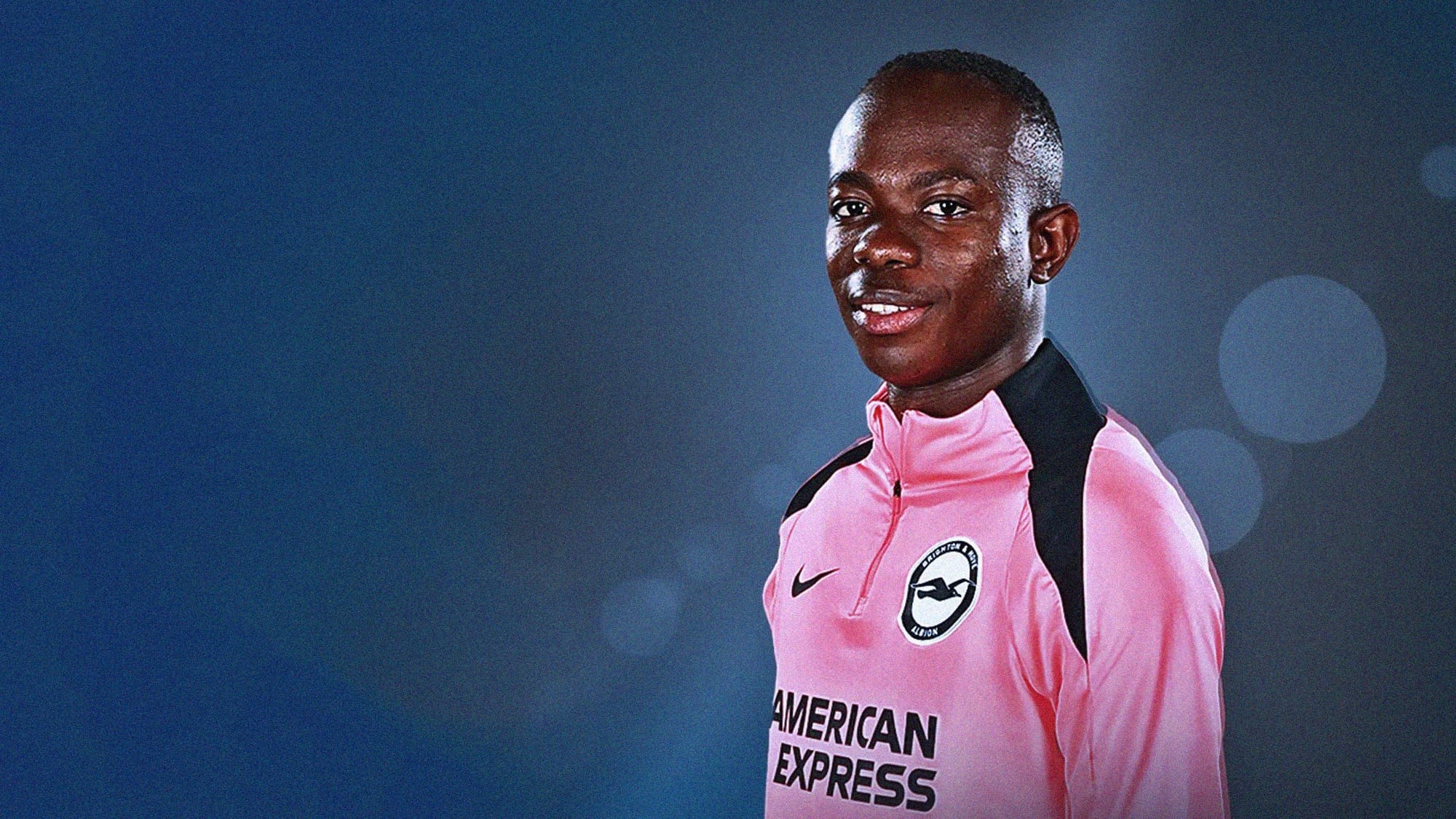 A photo of Malcik Junior Yalcouyé in a bright pink Brighton & Hove Albion t4raining jacket