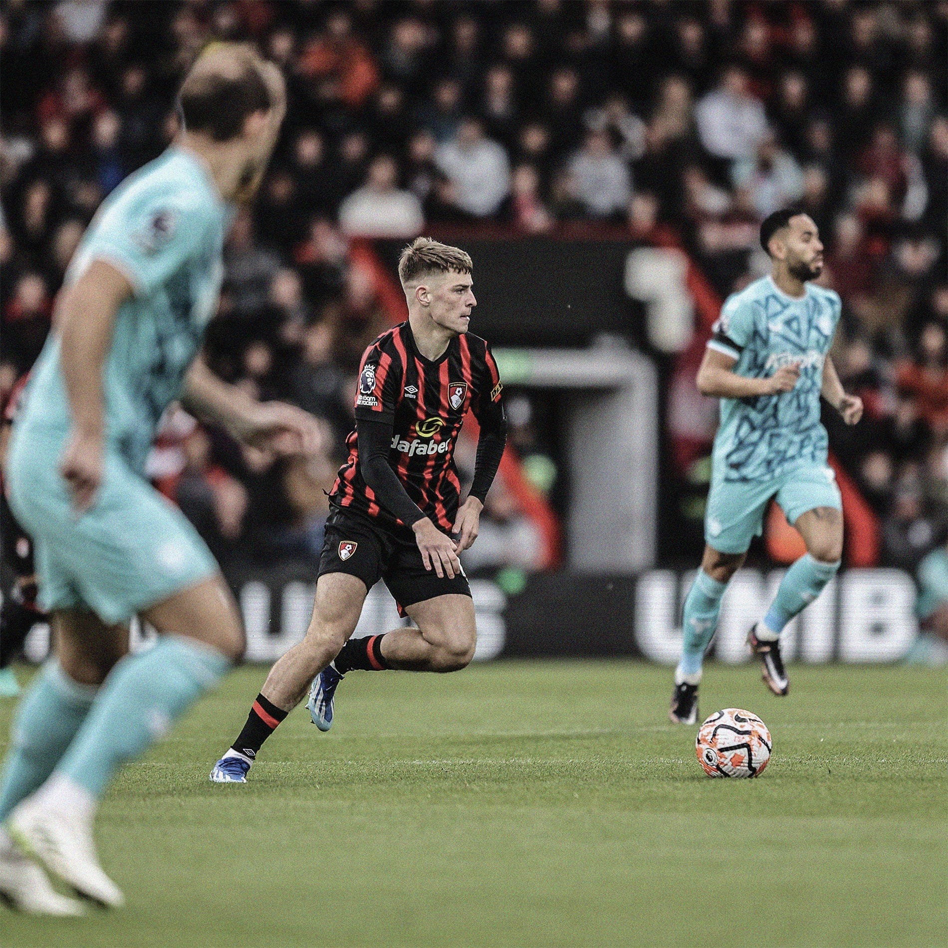 A photo of Alex Scott moving with the ball in midfield for Bournemouth in a Premier League game against Wolves. There are two Wolves players out of focus in the frame.