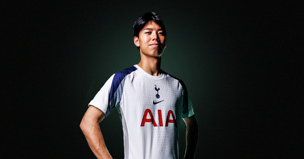 Kota Takai stood in a white-and-navy Tottenham Hotspur shirt, stood in front of a dark background with a green glow behind him