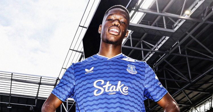 Thierno Barry wearing a blue Everton shirt, looking down at the camera with a stadium roof behind him